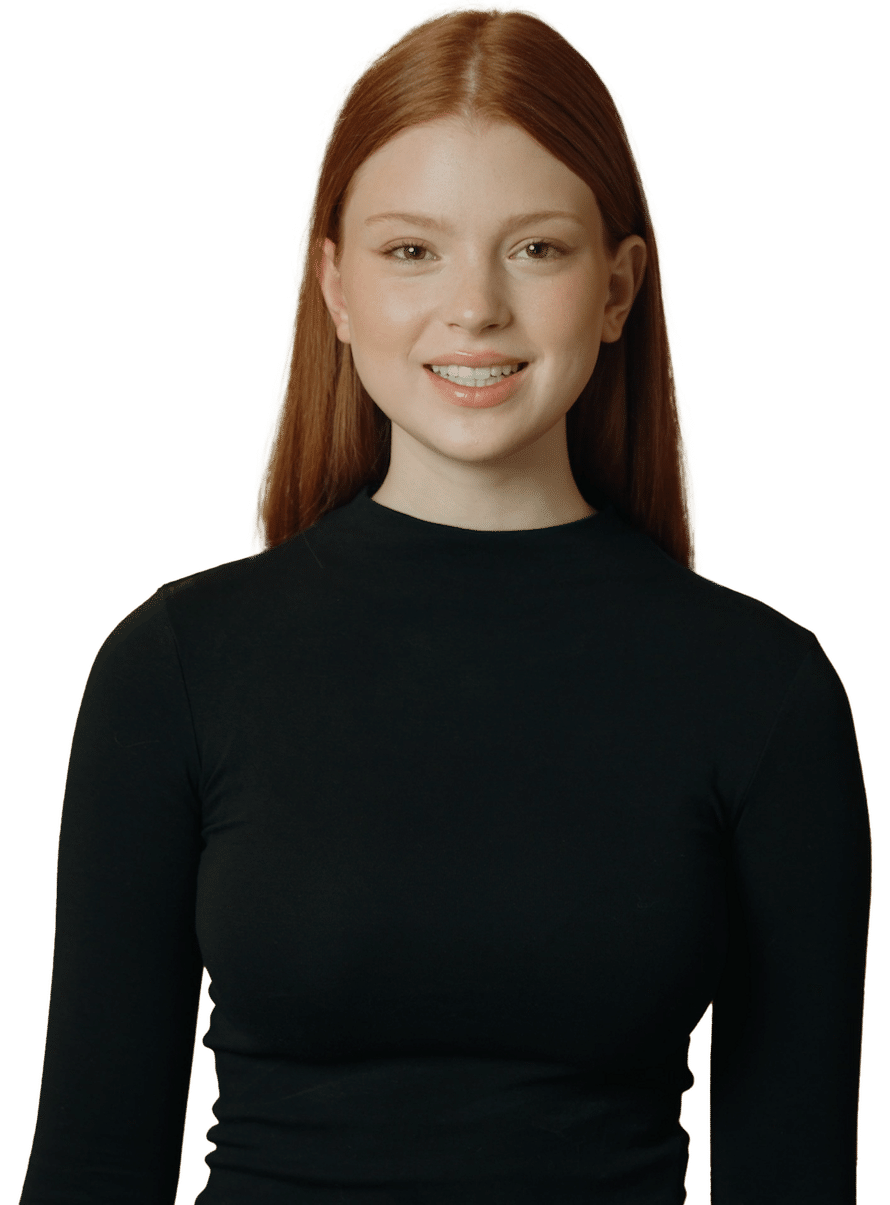 A young woman with straight, long red hair wearing a black long-sleeve top stands against a plain green background, smiling slightly at the camera—resembling the lifelike avatars created by D-ID Agents.